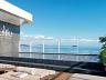 Piscina com deck elevado, espreguiadeiras sob o sol e vista para o mar.